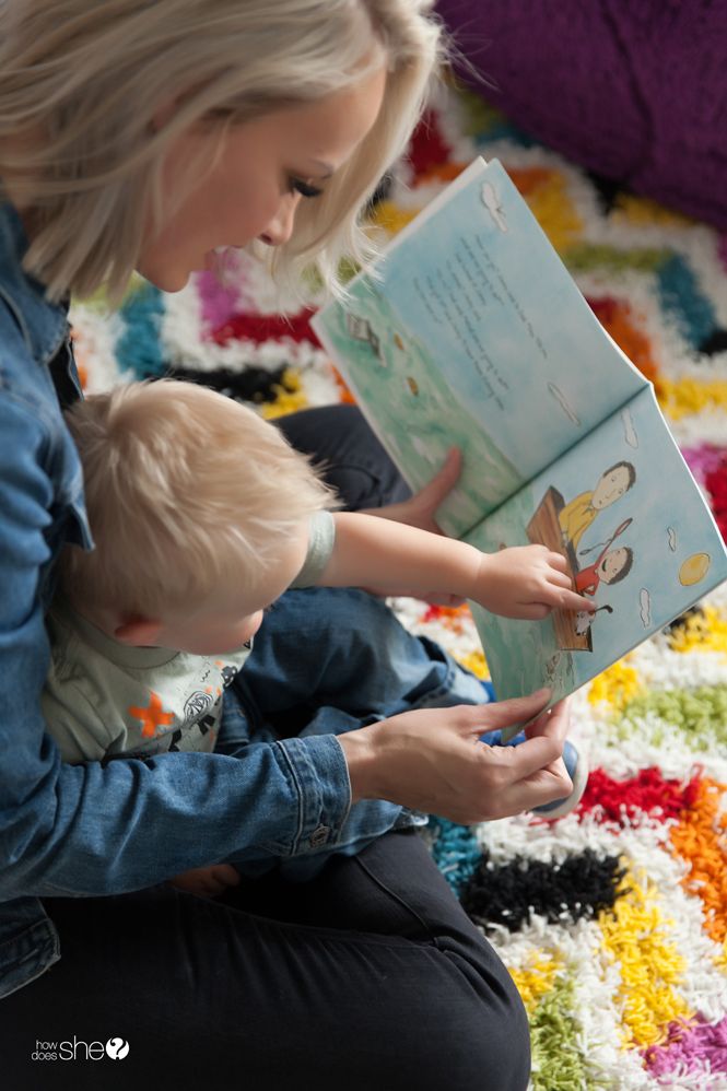 This may contain: a woman sitting on the floor reading a book to a child