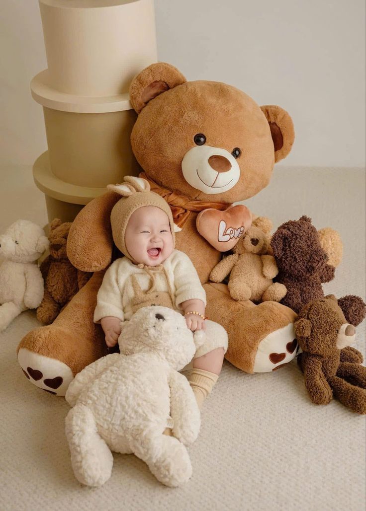 This may contain: a baby is sitting in between two large teddy bears and one smaller teddy bear on the floor