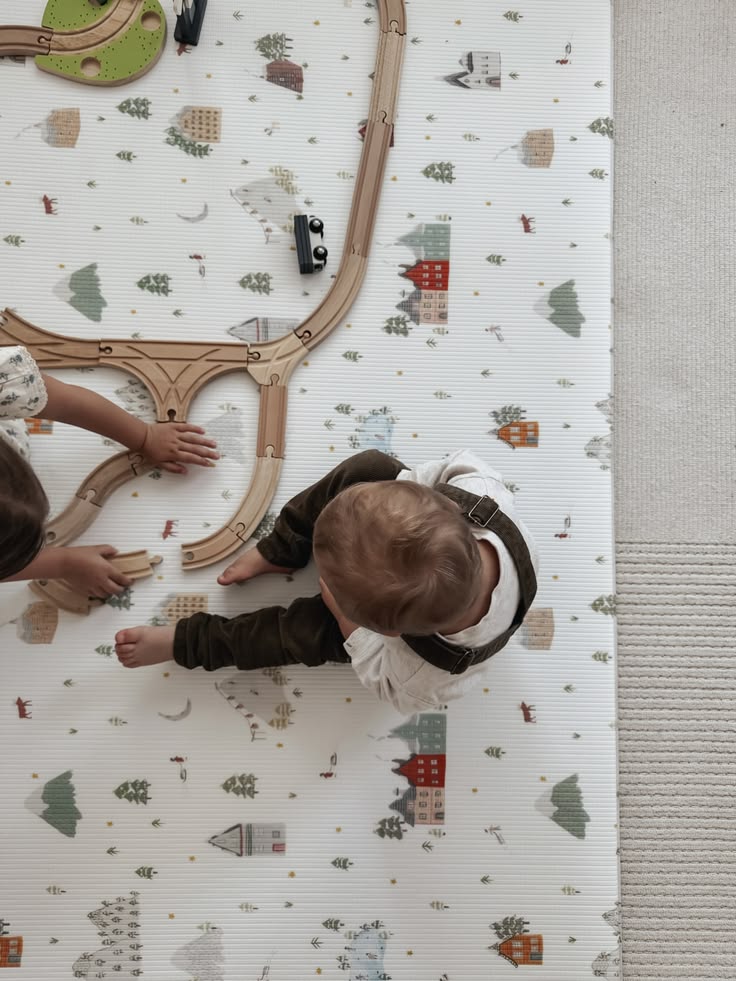This may contain: two toddlers playing with a toy train set on the floor in front of a wall