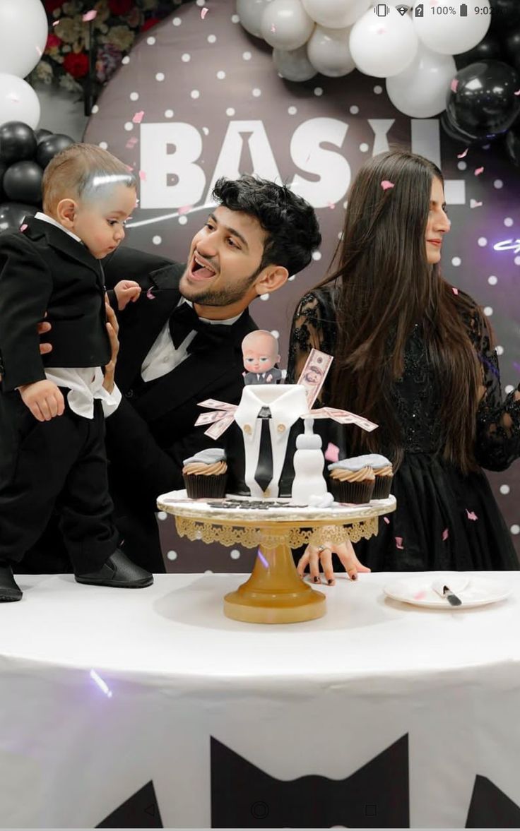 This may contain: a man and woman holding a baby in front of a cake
