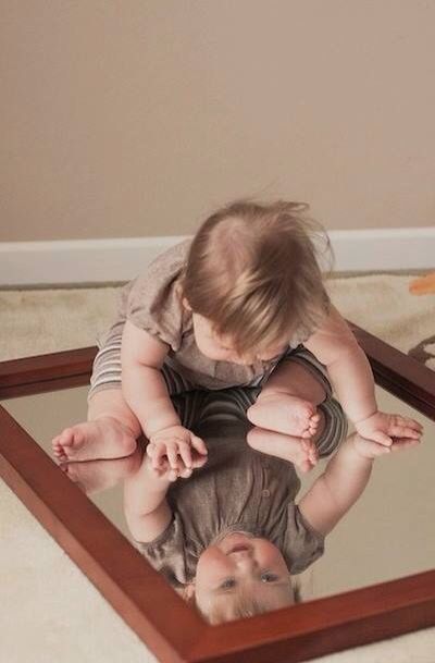 This may contain: a baby is looking at himself in the mirror while holding it's head up