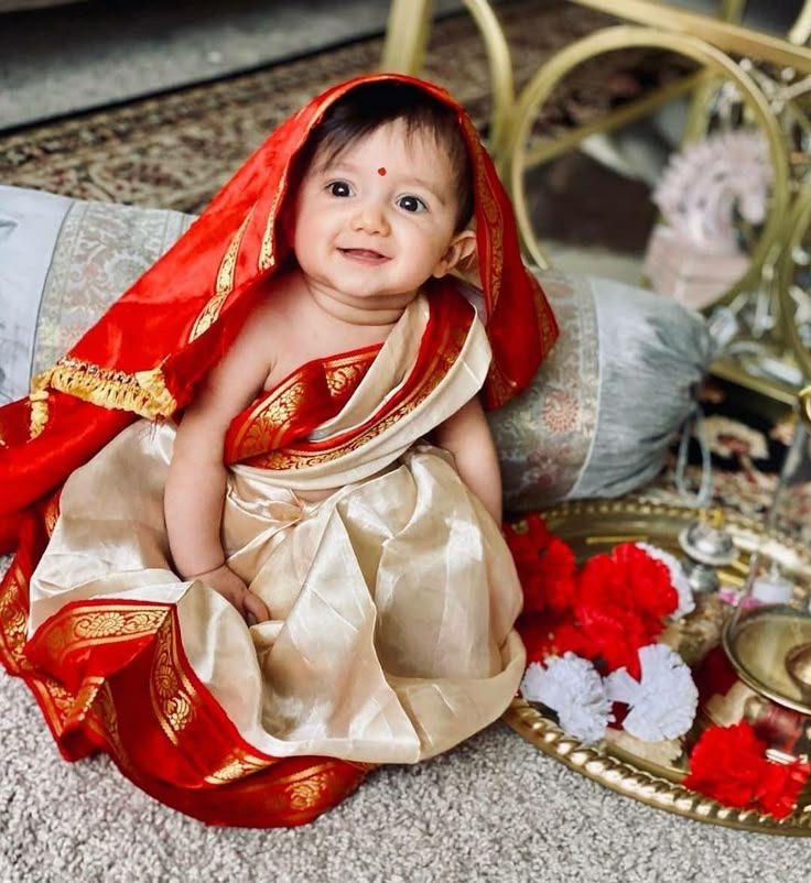 This may contain: a baby dressed in a red and gold outfit sitting on the floor next to a plate
