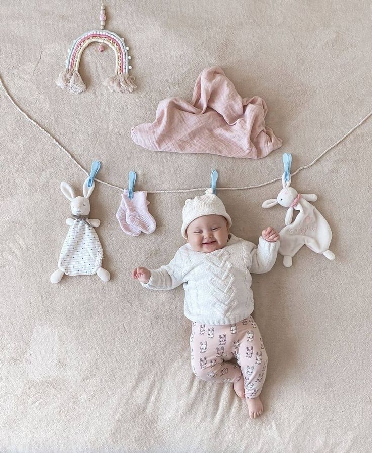 This may contain: a baby laying on top of a bed next to stuffed animals and clothes hanging from a line