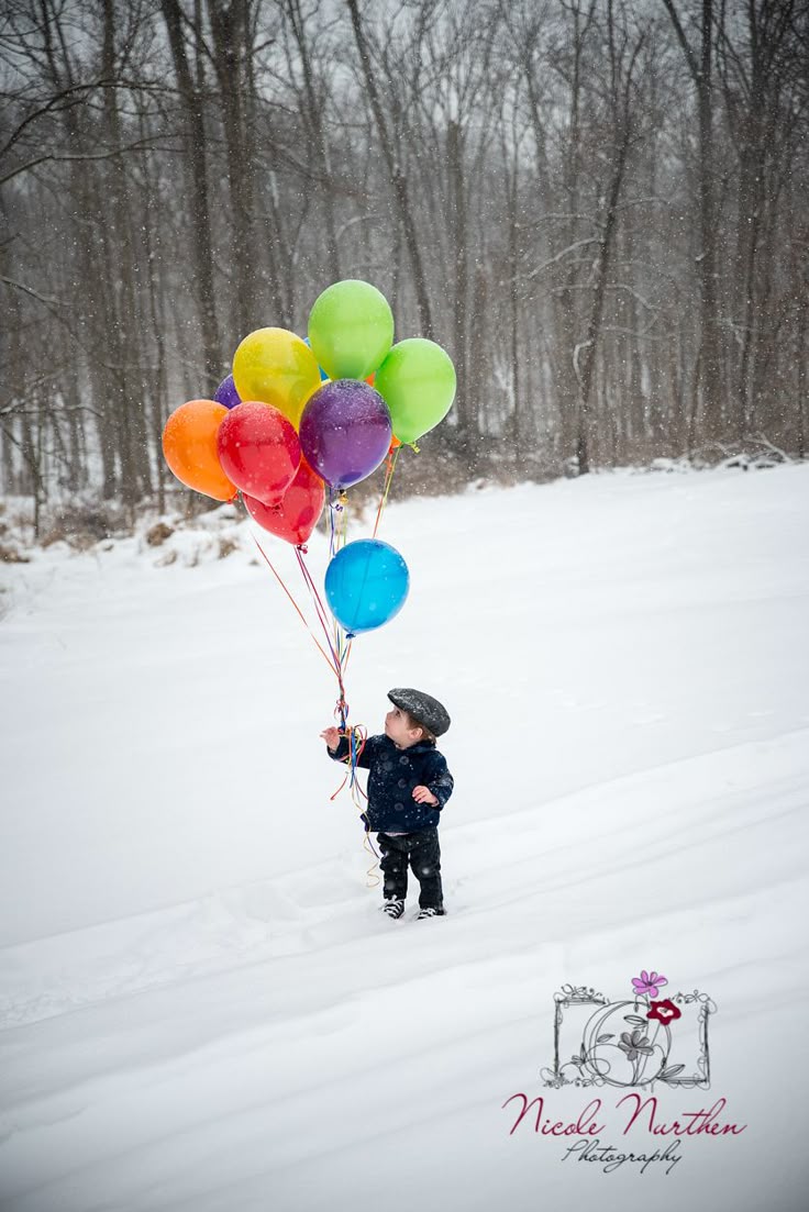 This may contain: a little boy holding onto some balloons in the snow