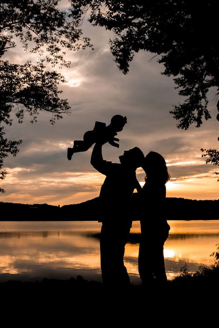 This may contain: a man holding a child in his arms as the sun sets