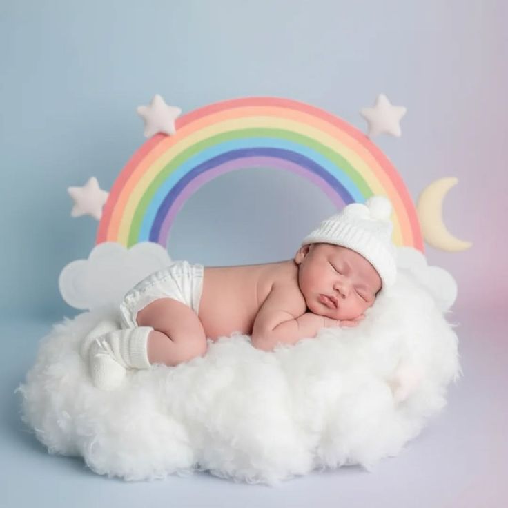 This may contain: a baby is sleeping on a cloud with a rainbow in the background