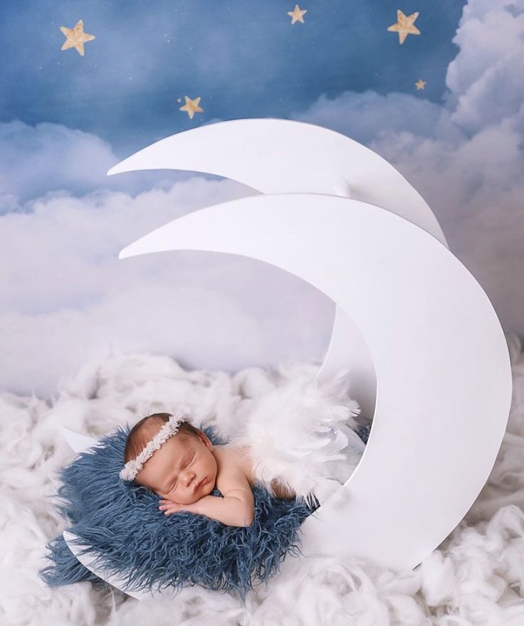 This may contain: a baby sleeping on top of a blue blanket in front of a white crescent with stars
